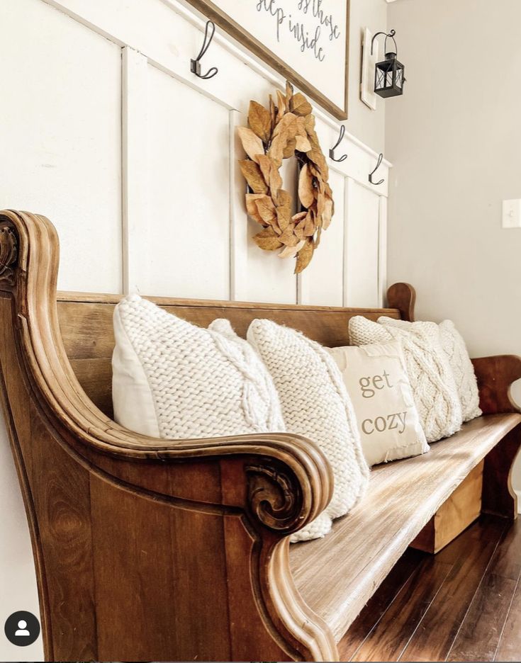 a wooden bench with pillows on it in front of a wreath and other items hanging on the wall