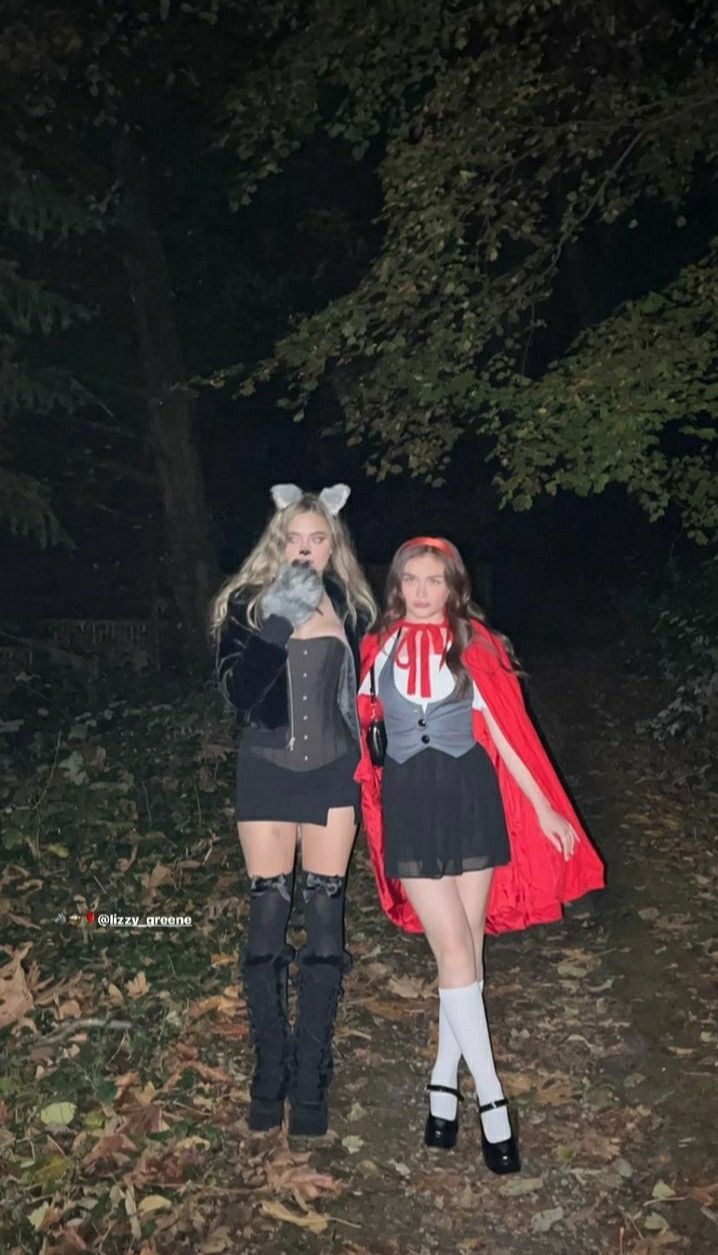 two women dressed up in costumes standing next to each other on a forest path at night