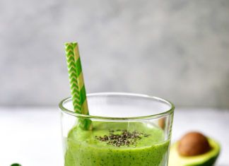 a green smoothie in a glass next to an avocado