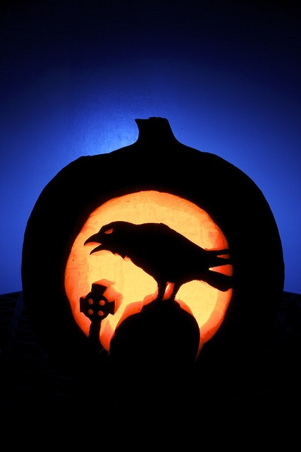 a pumpkin carved to look like a crow with a cross in the center and a full moon behind it