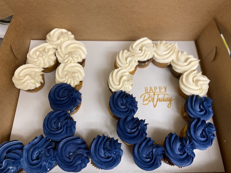 two blue and white cupcakes in a box with happy birthday written on it