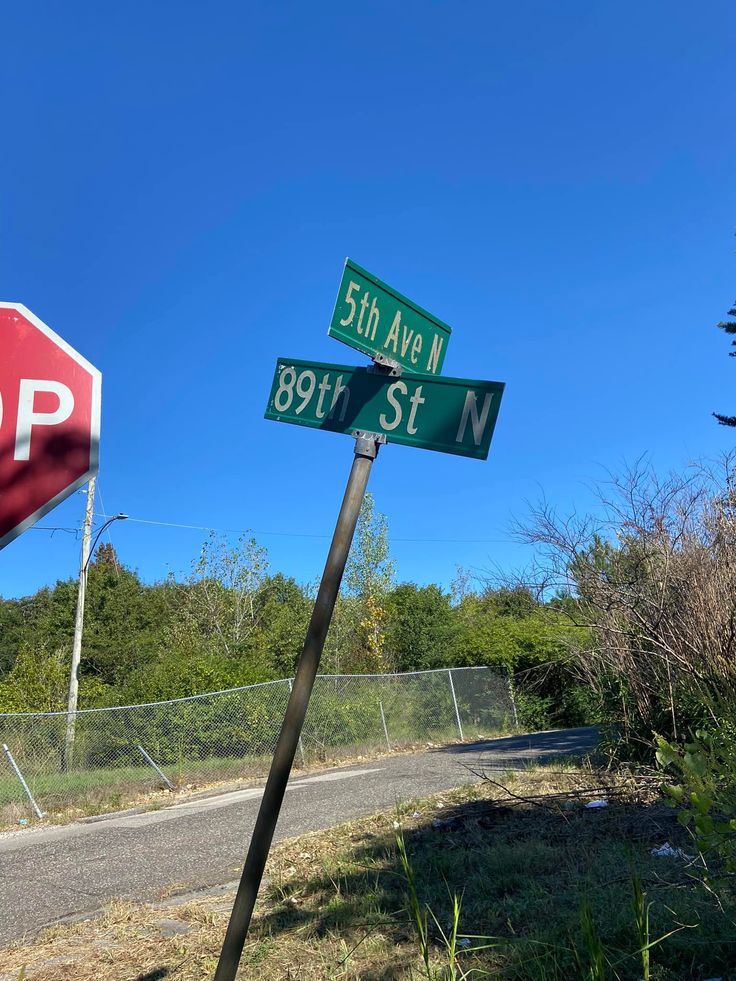 a stop sign and street signs in front of a fenced off area with trees