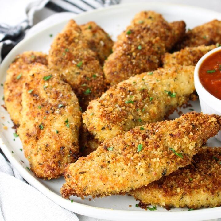 some fried food on a white plate with ketchup and dipping sauce in the bowl