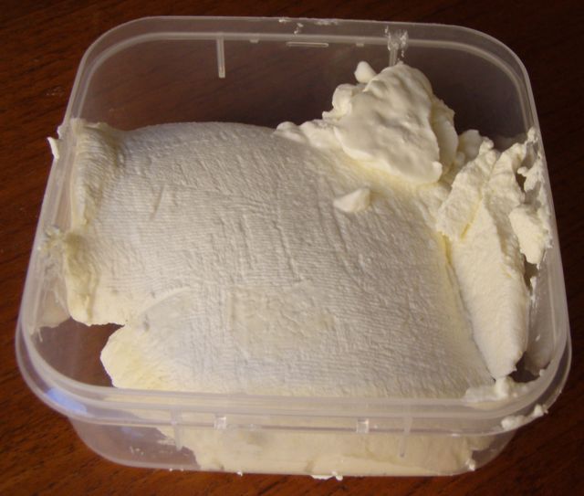 a plastic container filled with whipped cream on top of a wooden table