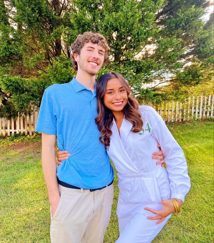 a young man and woman standing next to each other in front of a white picket fence