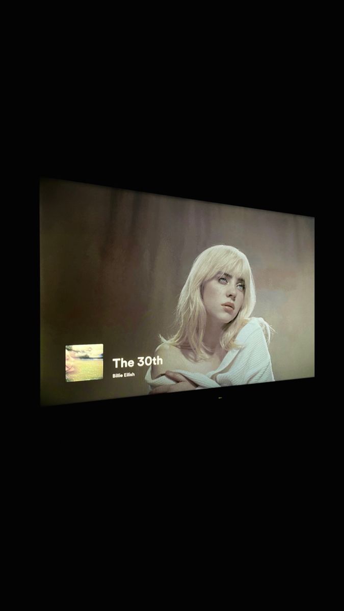 a woman with blonde hair standing in front of a large screen tv that reads the 30th anniversary album