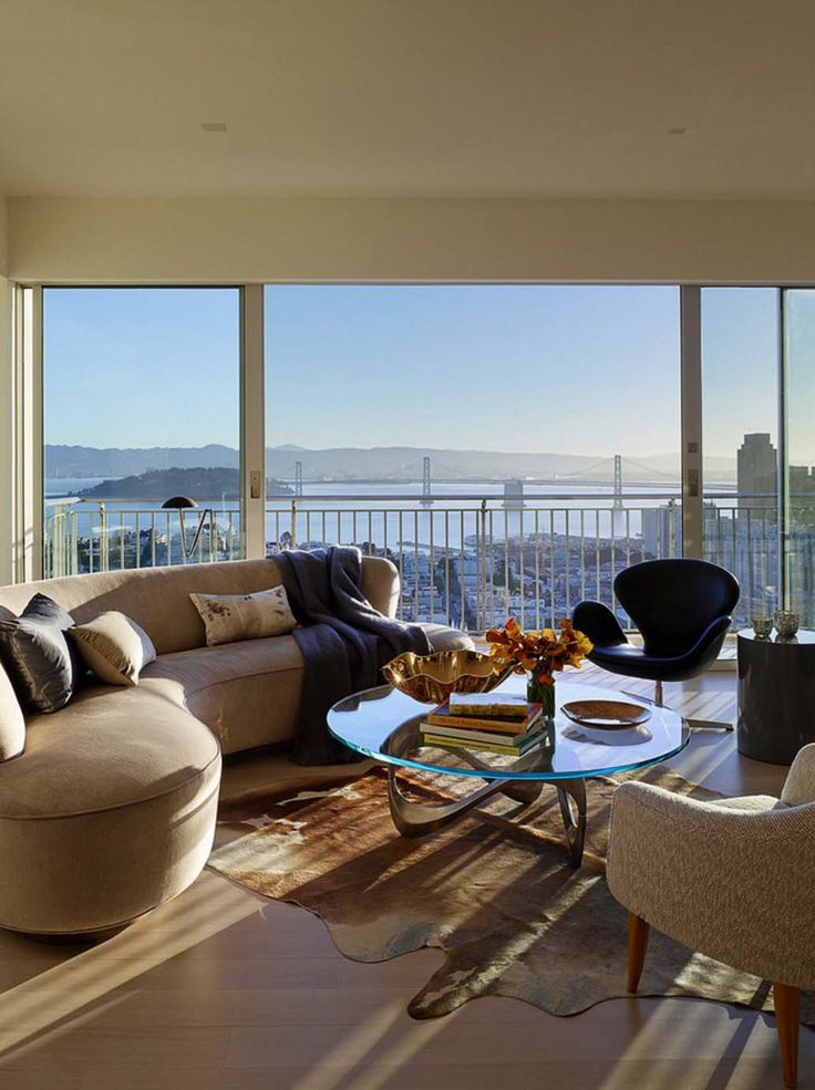 a living room filled with furniture and large windows overlooking the cityscape in the distance