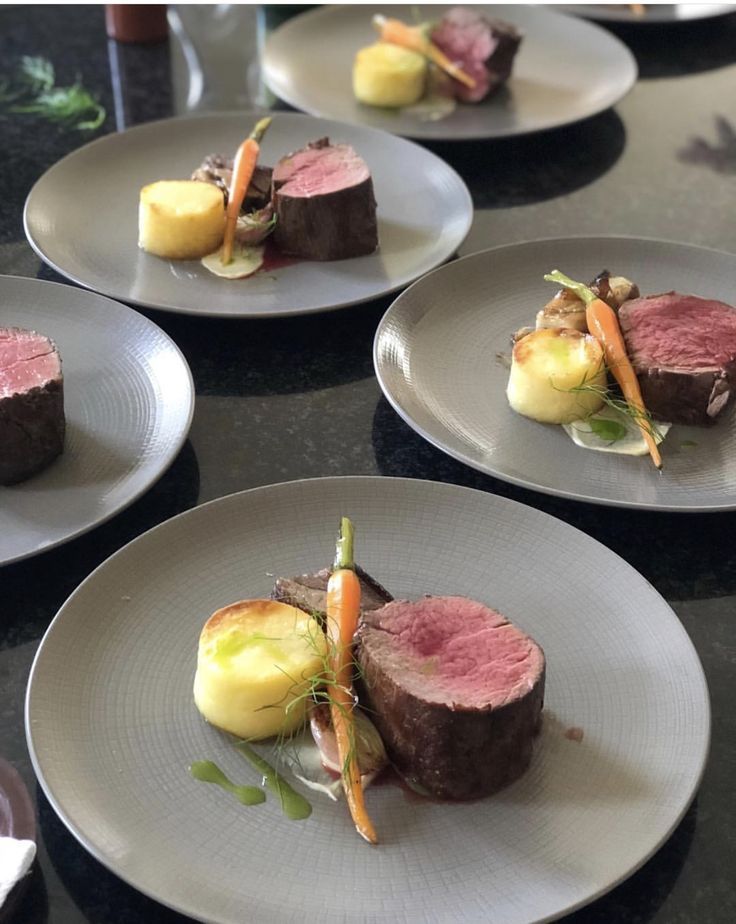 four white plates with different types of food on top of each one, including meat and vegetables