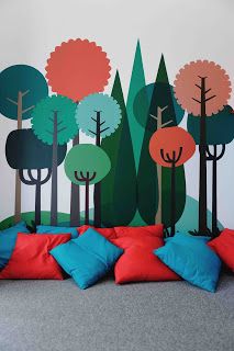 a bed with pillows on it in front of a wall painted with trees and bushes