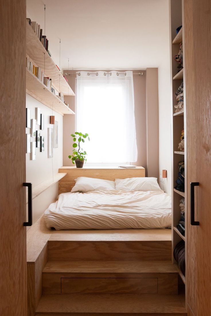 a bed sitting under a window next to a wooden shelf