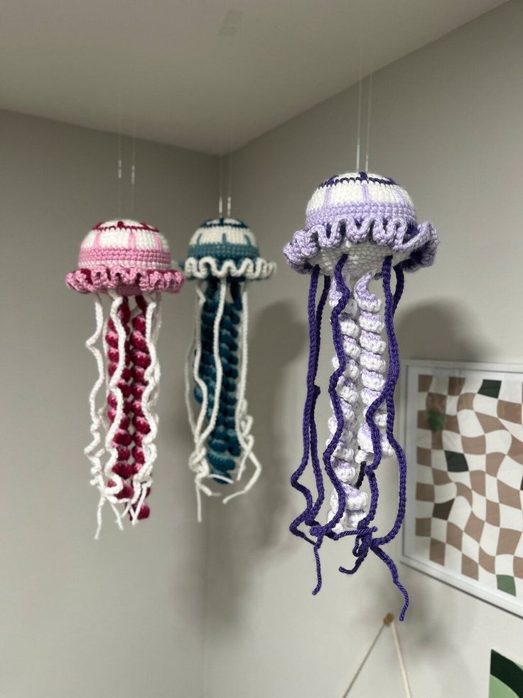 three crocheted jellyfish hanging from the ceiling in a room with white walls