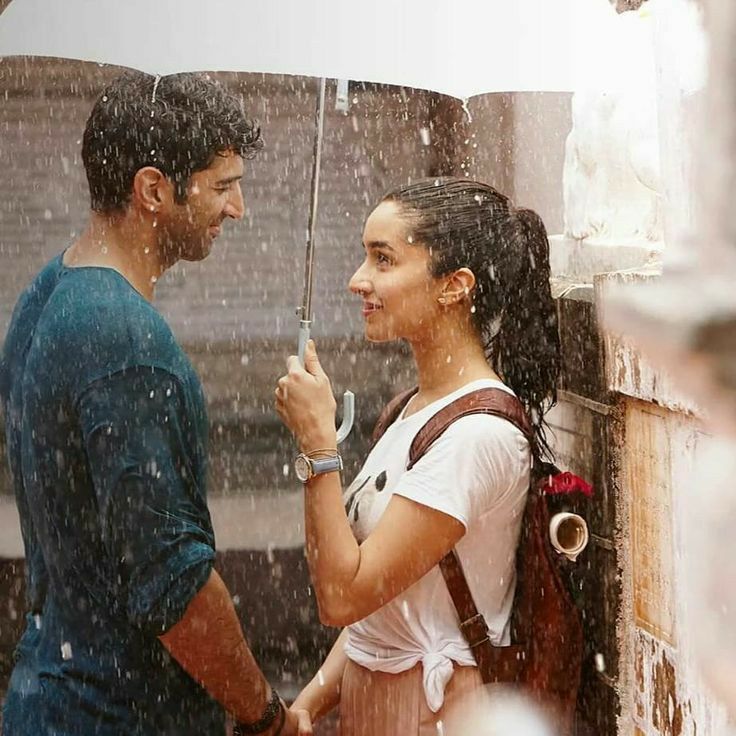 a man and woman standing under an umbrella in the rain, looking at each other