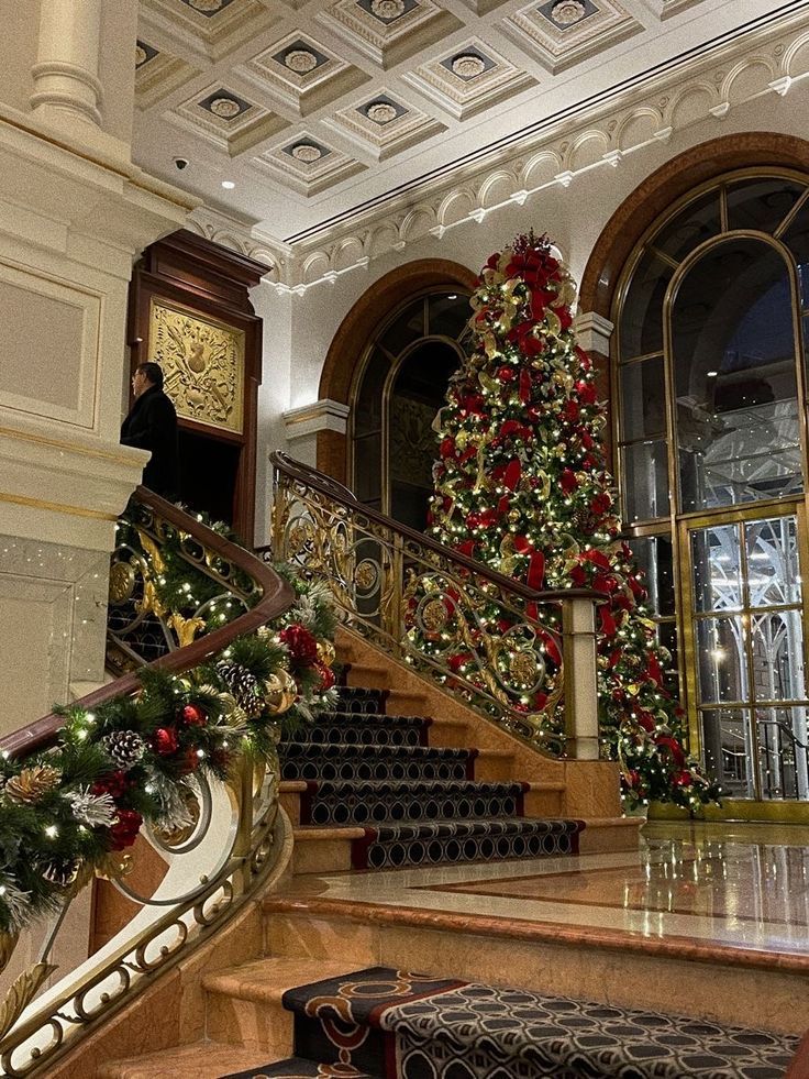 christmas decorations are on display in the foyer of a building with staircases and decorated trees