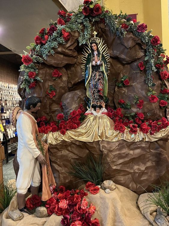 a statue of the virgin mary surrounded by red flowers and greenery in a store