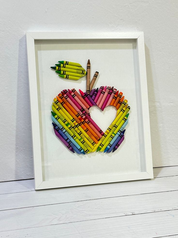 an apple made out of crayons in a white frame