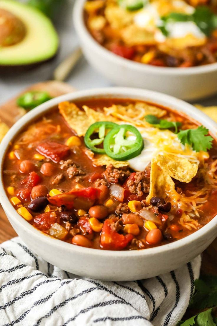 two bowls filled with chili, beans and tortilla chips on top of a cutting board