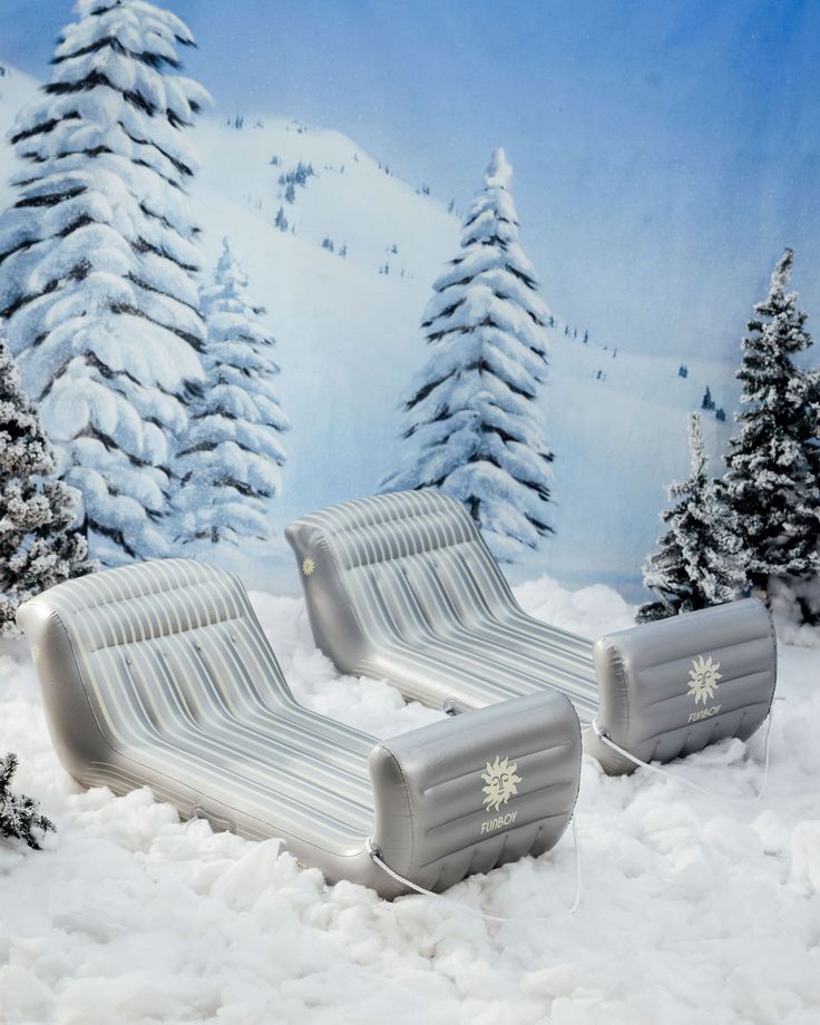 two inflatable lounge chairs sitting on top of snow covered ground next to trees