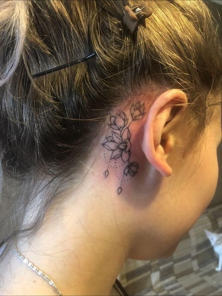 a woman with a flower tattoo on her left side behind the ear is looking down