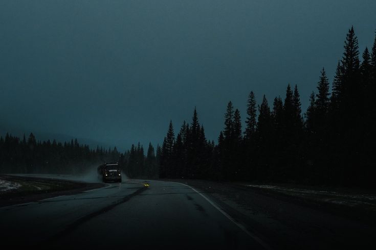 a car driving down a road in the dark with trees on both sides and an overcast sky