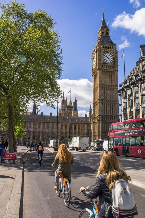 two women riding bicycles down the street in front of big ben