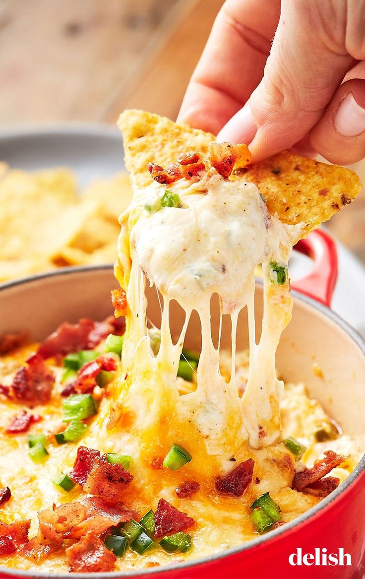 a person is taking a slice of pizza from a red casserole dish with cheese and green onions