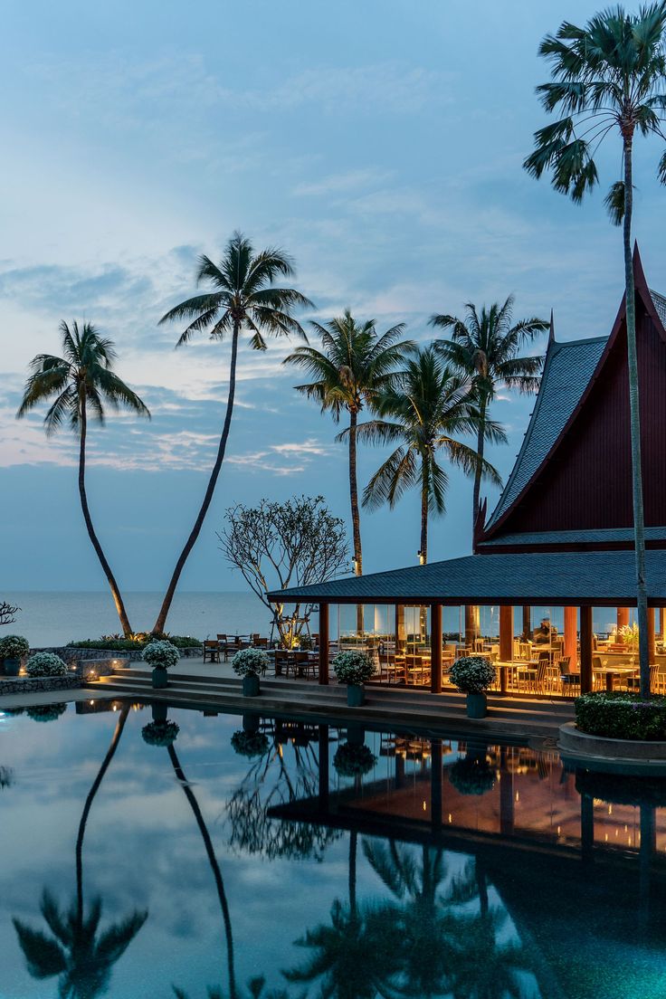 an outdoor restaurant with palm trees and the ocean in the background at dusk, surrounded by water