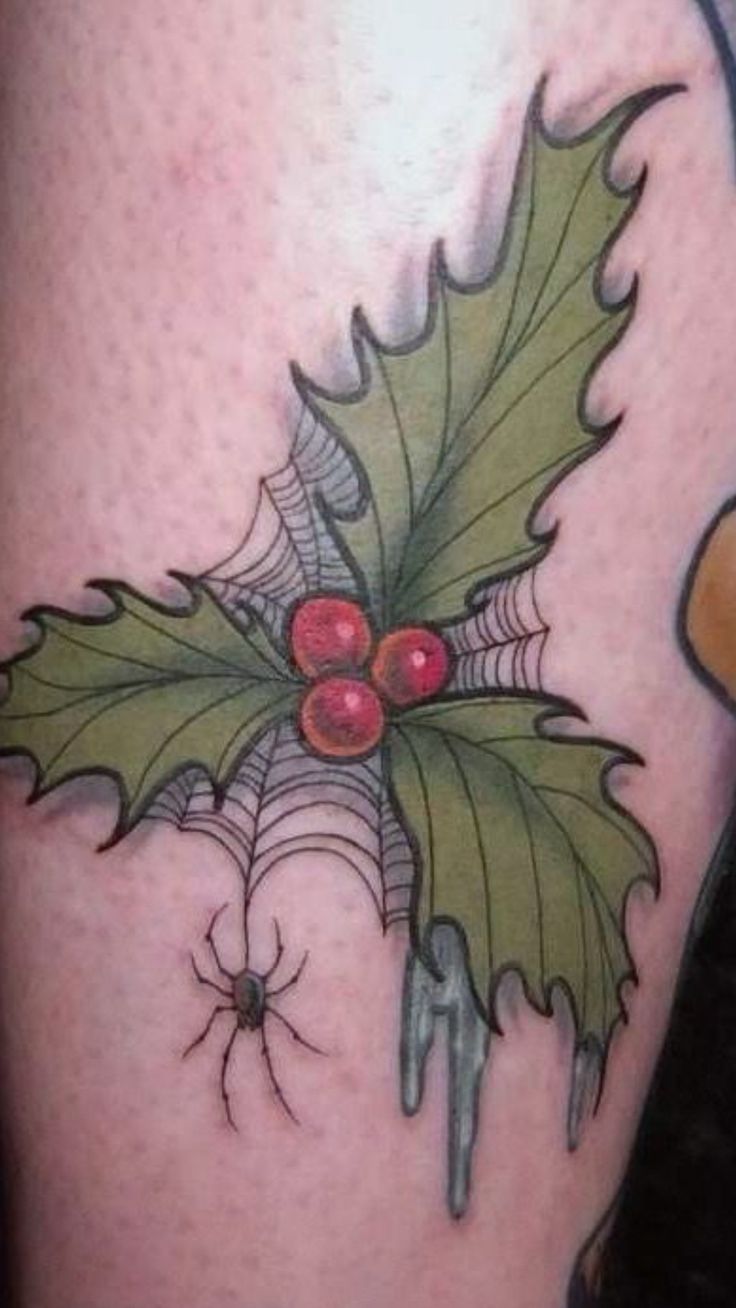 a tattoo with holly leaves and spider webs on the thigh, as well as red berries