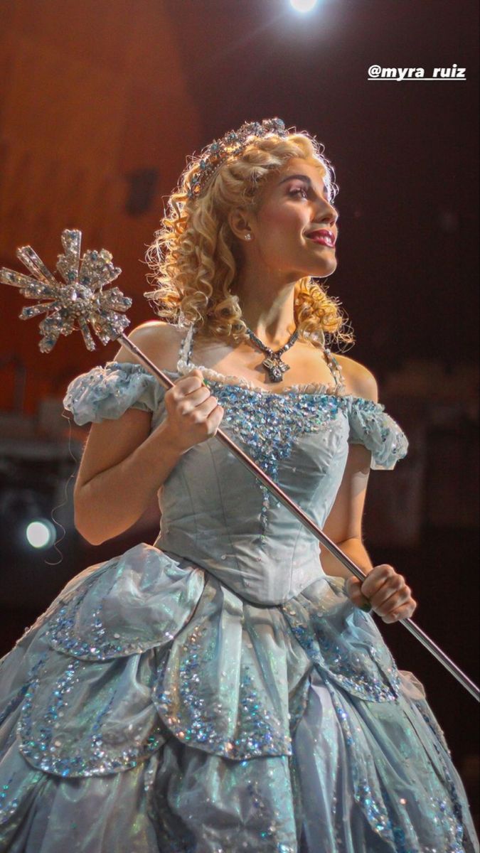 a woman in a blue dress holding a snowflake on her shoulder and wearing a tiara