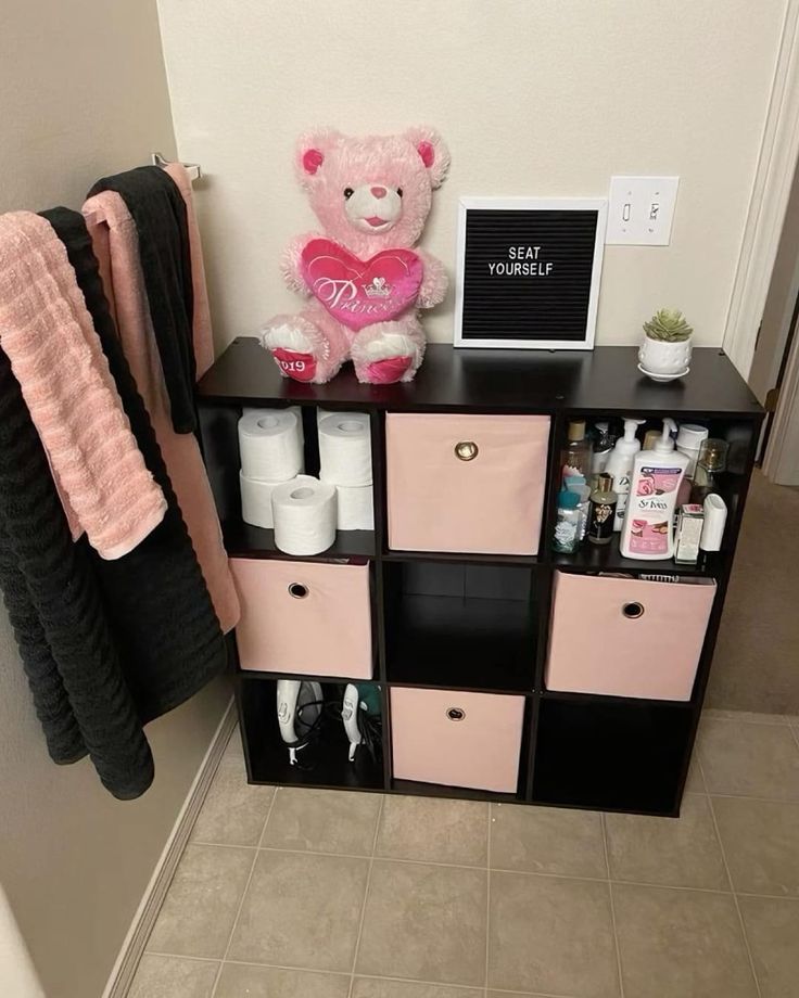 a pink teddy bear sitting on top of a black shelf next to some toiletries