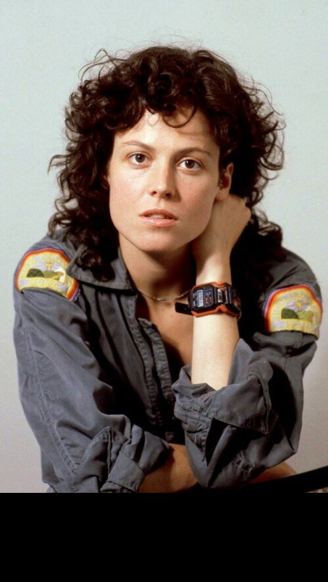 a woman with curly hair wearing a watch and looking off to the side while leaning on her hand