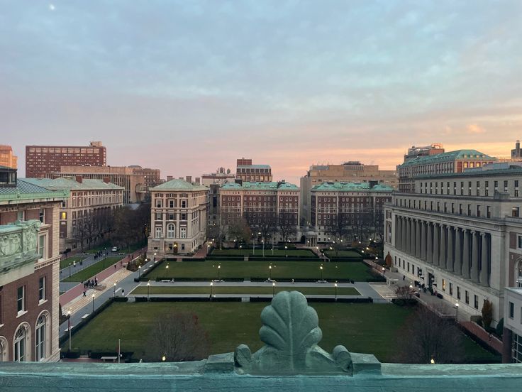 an aerial view of a city with buildings and a lawn in the foreground at sunset