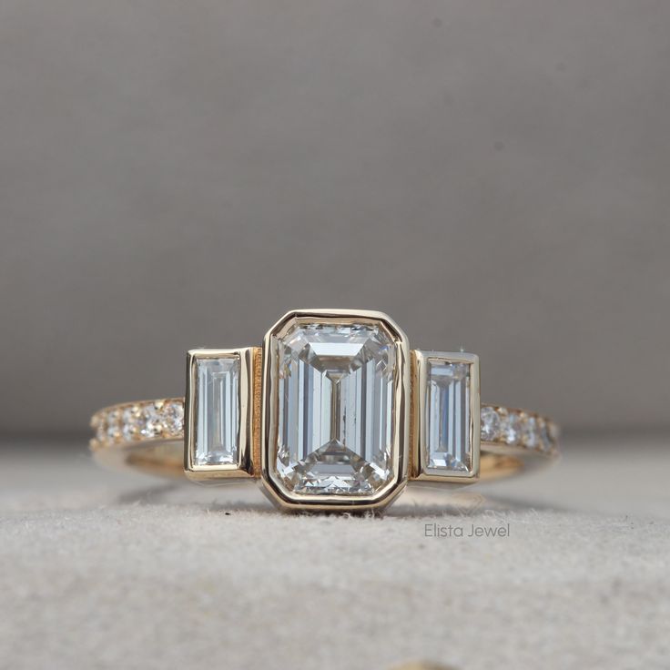 Emerald Cut Lab Diamond Three Stone Engagement Ring By Elista Jewel ✨ Diamond Details ✨ ↦ Total Diamond Weight: 1.24Carats ↦ Center Diamond Shape: Emerald Cut ↦ Center Diamond Weight: 0.90 CT ↦ Accent Diamond Shape: Emerald & Round Cut ↦ Accent Diamond Weight: 0.34 CT ↦ Color: H ↦ Clarity: VS2 ↦ Setting: Prong ↦ Ring Size: Size Selectable This lab-grown diamond was grown by the CVD /HTHP process. ✨ Jewelry Details ✨ ↦ Metal Purity: Solid Gold (10KT, 14KT, 18KT); 950 Platinum ↦ Metal Tone: Yellow, White, Rose ↦ Stamp/Hallmark: Yes ↦Center Stone Certificate: IGI / GIA Certified Diamond ↦ Jewelry Certificate: Free of Cost with Listed Design ↦ SKU No: LR-10317 ✨ Specialty and Notes: ▪ Customized Designer Jewelry. ▪ Since we make our own Diamonds, any kind of customization can be made to them. Art Deco 14k Gold Jewelry With Bezel Setting, 14k Gold Three Stone Baguette Cut Jewelry, Gold Three Stone Jewelry For Anniversary, Gia Certified 14k Gold Jewelry For Anniversary, 14k Gold Jewelry With Bezel Setting For Anniversary, 14k Gold Art Deco Jewelry With Vvs Clarity, Emerald Cut Bezel Setting Anniversary Jewelry, Gia Certified Gold Baguette Cut Jewelry, Gia Certified Gold Jewelry With Baguette Cut