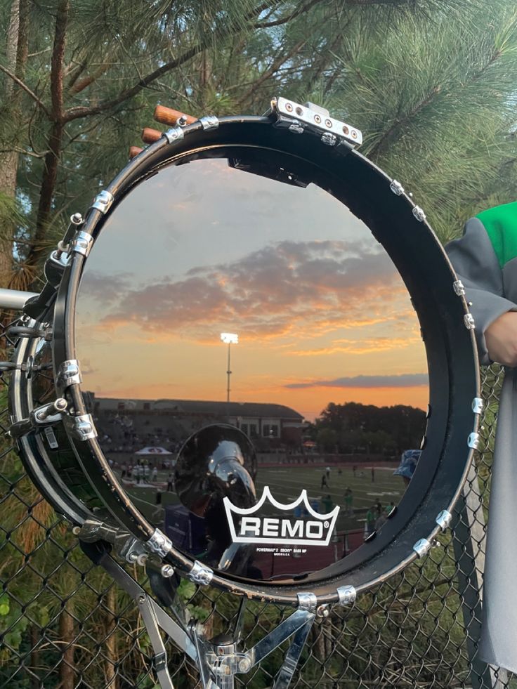 a man holding up a drum set in front of a fence with the sun setting behind it