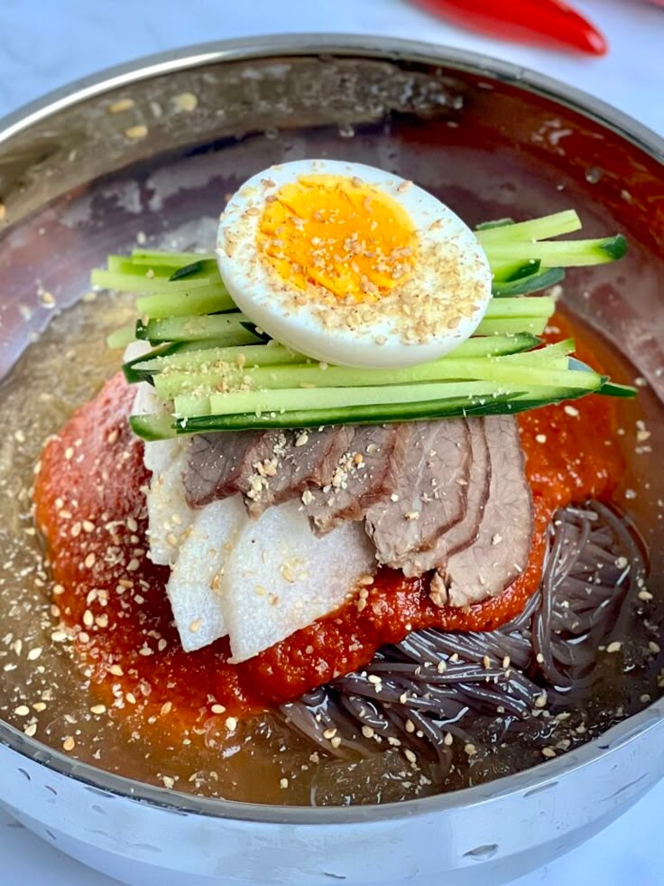 a metal bowl filled with meat and an egg on top of it's side