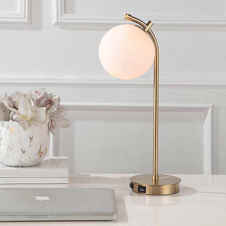 a table lamp sitting on top of a white desk next to a laptop computer and flowers