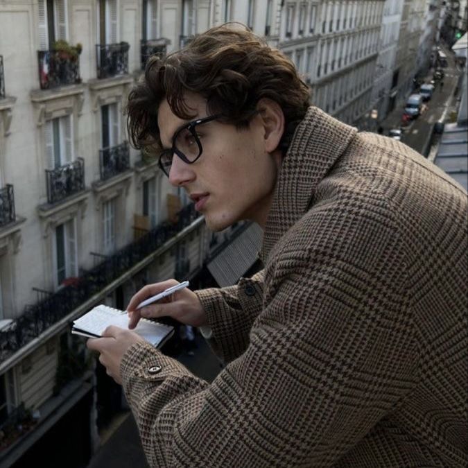 a man with glasses looking at something on his cell phone in front of some buildings