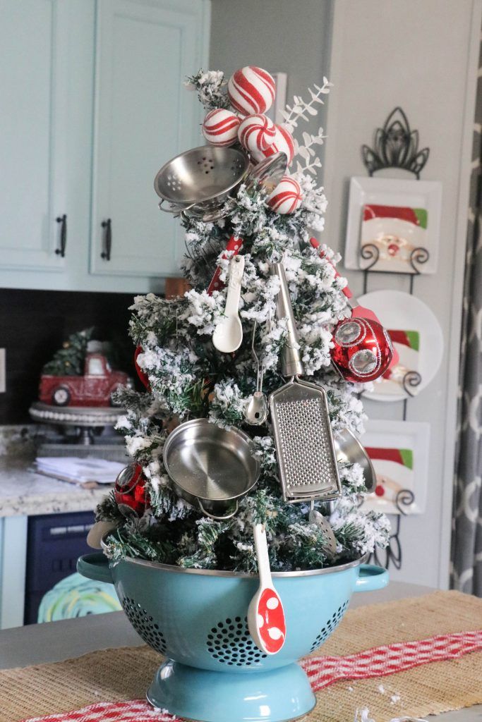 a decorated christmas tree with utensils in a colander on a kitchen counter