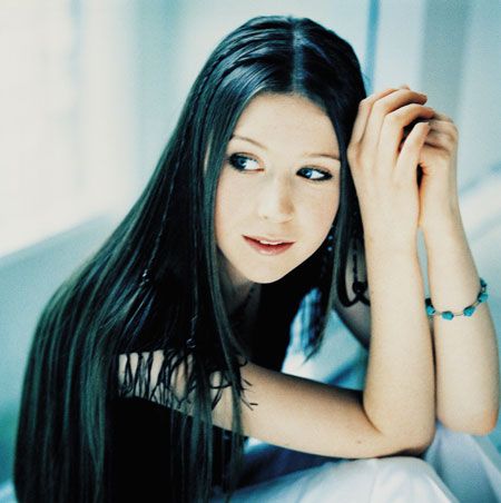 a woman with long black hair laying on top of a bed