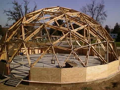 a large wooden structure sitting on top of a dirt field in front of a forest