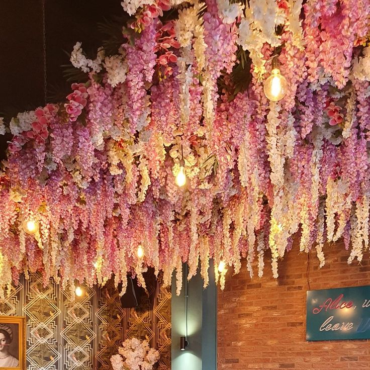 pink and white flowers hanging from the ceiling in front of a wall with pictures on it