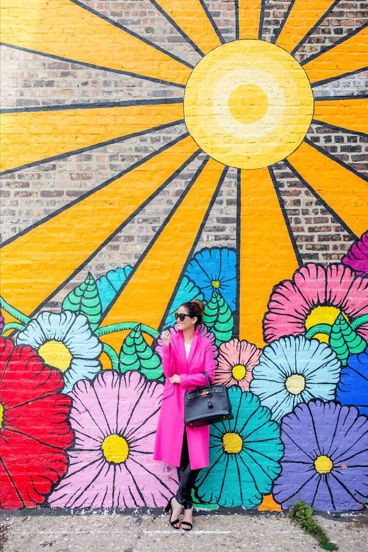 a woman standing in front of a colorful wall painted with flowers and sunbursts