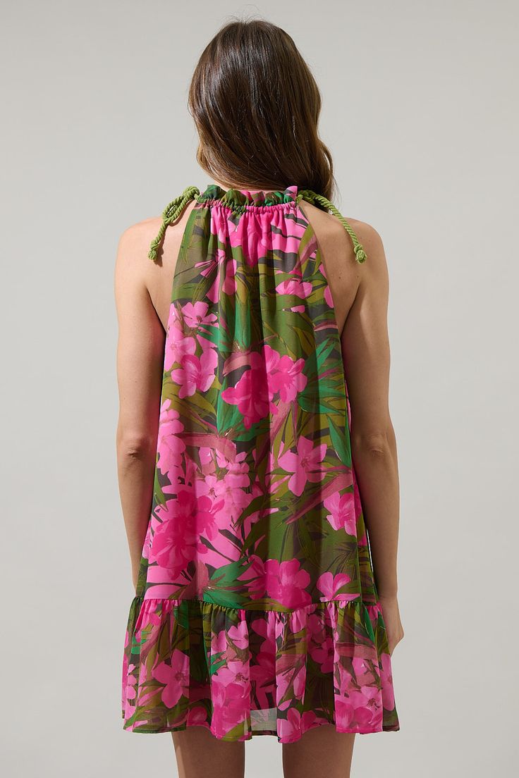 Bring the Dandi Floral Rumba Halter Mini Dress to your next vacation. An extra cute pink floral print designs this mini dress with a ruffle trim high neckline with a halter style. Adjust the height slightly with adjustable tie strings. The dress maintains an A line silhouette with a ruffle tier hem. Wear it with pink strappy heels. - Adjustable straps- Shift silhouette- Halter neck- Lined- Color: Green Pink CoralSize + Fit - Model is 5'8" and wearing size XS- Measurements taken from size S - Che Vacation Mini Dress With Elastic Neckline, Pink Hibiscus Print Summer Dress, Green Tropical Halter Neck Dress, Pink Ruffled Halter Neck Sundress, Pink Sleeveless Tropical Sundress, Pink Hibiscus Print Dresses For Spring, Tropical Halter Neck Dress For Garden Party, Pink Halter Neck Mini Dress With Ruffles, Feminine Pink Halter Dress For Vacation