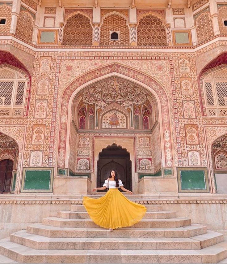 a woman in white shirt and yellow skirt standing on steps with stairs leading up to an ornate building