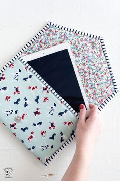 a person holding an ipad on top of a cloth covered case with flowers and dogs