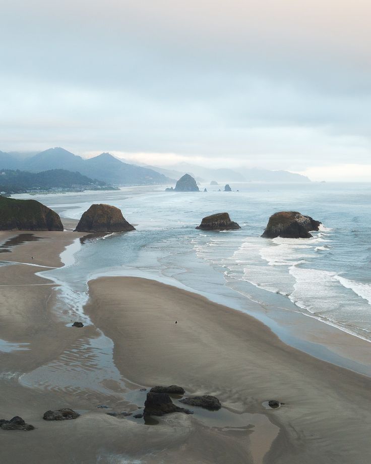 the beach is covered in sand and water as waves crash on top of rocks, with mountains in the distance