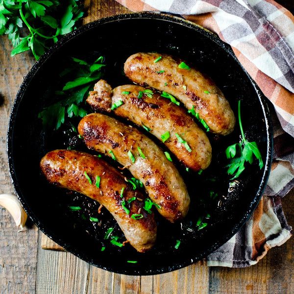 four sausages in a skillet on a wooden table with garlic and parsley