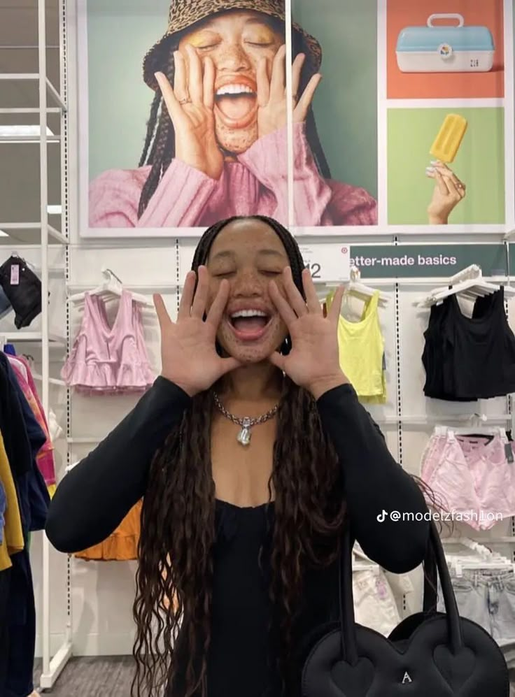 a woman holding her hands up to her face while standing in front of clothing racks