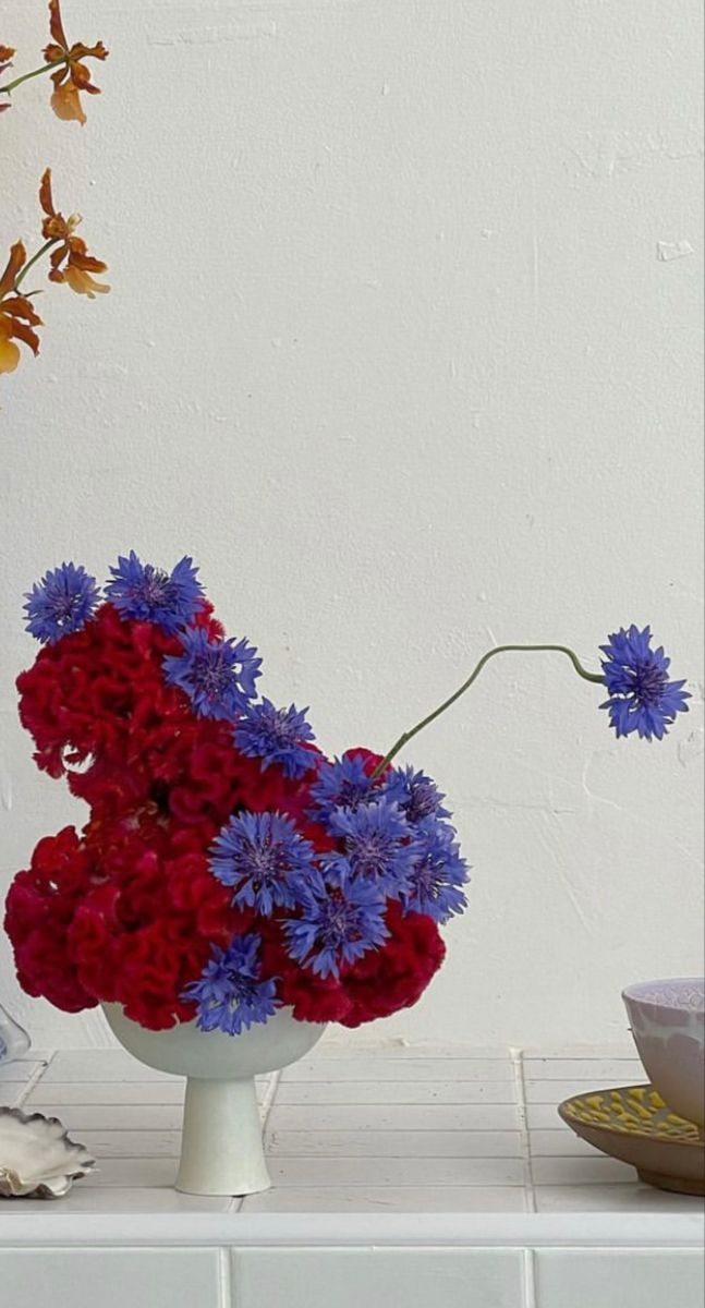 red, white and blue flowers are in a vase on a counter next to an empty bowl