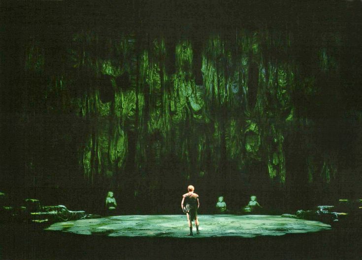 a man standing on top of a stage in front of a giant green forest wall