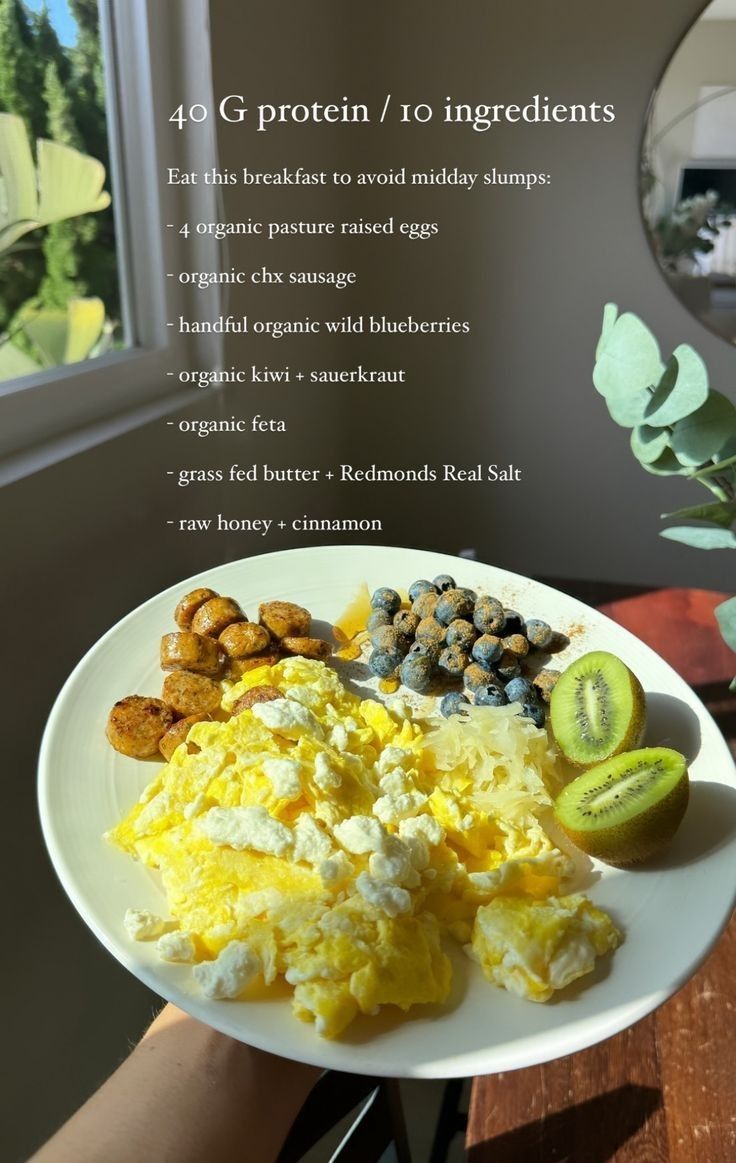 a white plate topped with eggs and other foods on top of a wooden table next to a window